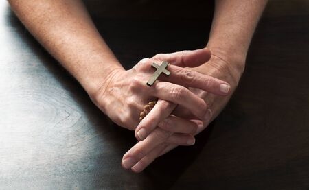 talking hands concept - female hands holding a religious cross praying for confession on dark wooden...