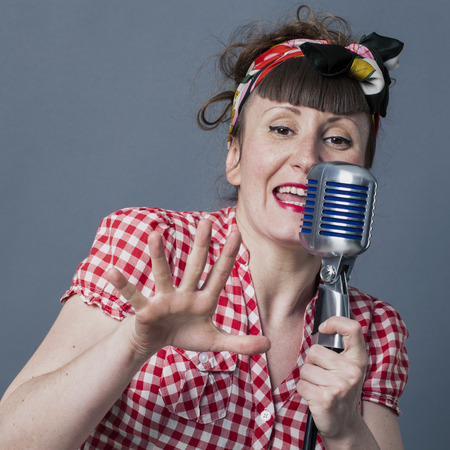 fifties singer in studio - 30s female performing artist with retro style singing in old fashioned microphone, closeup over gray backgroundの写真素材