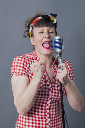 fifties singer in studio - passionate young woman with retro style singing in old fashioned mike, gray backgroundの写真素材