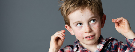 innocent thinking - closeup portrait of an adorable red hair little boy looking up, raising hands to...