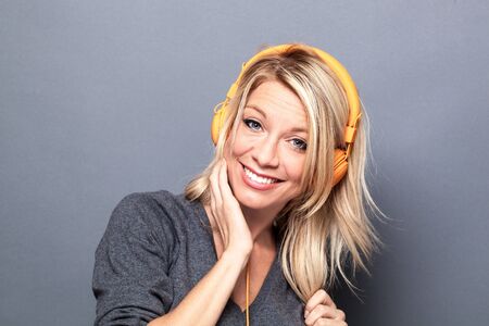 thrilled young blond woman listening to music on headphones for wellbeing, grey background studioの写真素材