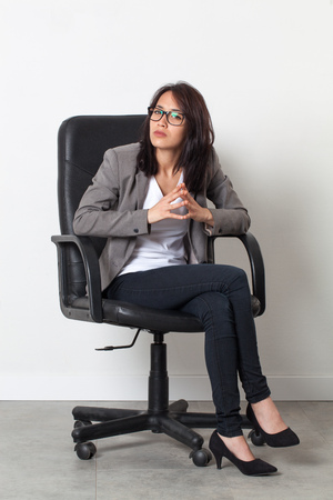 female self-employment - serious beautiful young businesswoman sitting in an office chair for her startup job over sparse white backgroundの写真素材