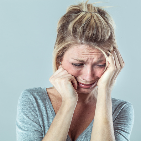 drama concept - depressed young blond woman in pain with big tears expressing her failure and sadness, grey background studio, contrast effectsの写真素材