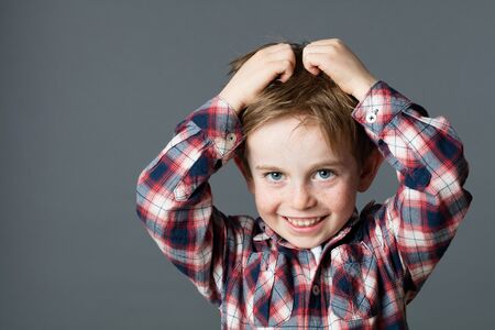 smiling young boy with freckles scratching his hair for head lice or allergies, grey background studioの写真素材