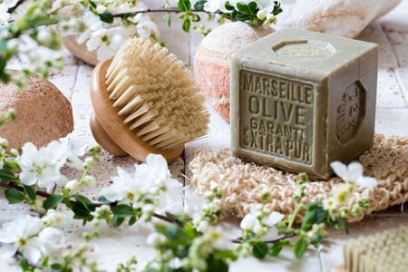 cleansing concept - beautiful body brush and organic olive oil solid soap with beige pebbles in fresh white spring blossom flowers for natural washing upの写真素材
