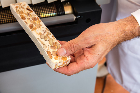 professional hands showing a hand-made French almond and honey nougat portion freshly packed in cellophane for commercial useの写真素材