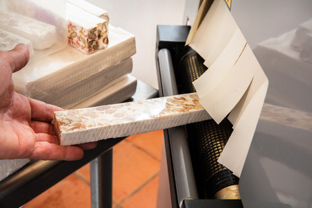 professional hands making hand-made French almond and honey nougat bar to pack in cellophane for commercial useの写真素材