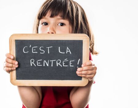 shy young girl playing hide and seek behind a writing slate, warning about a scary back to school, white background studioの写真素材