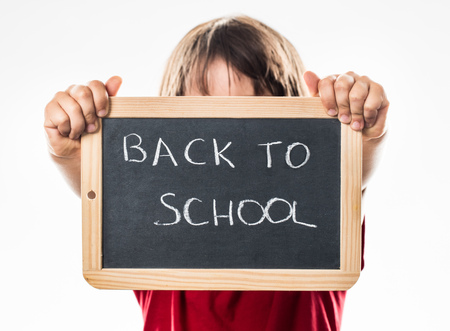 anonymous little kid announcing a proud back to school in holding a writing slate in the foreground, white background studioの写真素材
