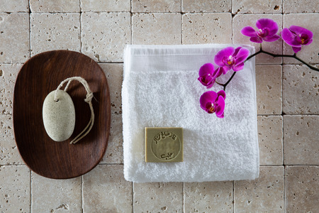 foot care concept with pumice stone, Alep soap, white cotton towel with pink orchid set on natural beige limestone for exfoliation spa, flat lay, top viewの写真素材