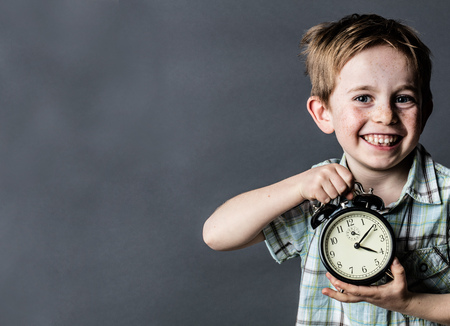 giggling young child with freckles and missing tooth enjoying showing an alarm clock for time concept and youth, grey background, retro contrast effects with copy spaceの写真素材