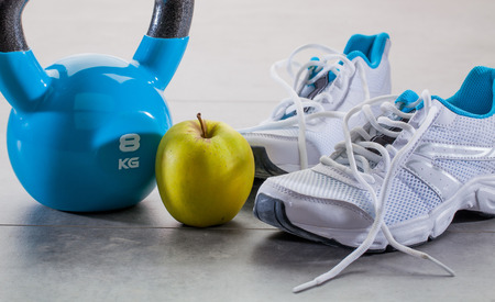 toning up exercise concept with gym sneakers, blue kettle bell and an apple for wellbeing lifestyle, aerobic still-life on grey floorの写真素材