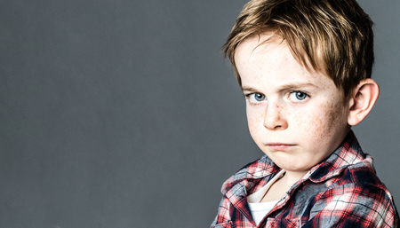 closeup of mad little boy with freckles standing from profile, pouting and sulking to express his attitude or frustration, contrast effects, copy spaceの写真素材