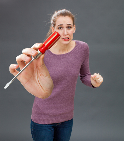 embarrassed young woman frowning with a symbolic screwdriver in hand to express her anxiety and stress at DIY, home improvement or repairing with industrial toolの写真素材