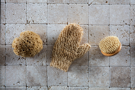 still-life of different exfoliating accessories with natural loofah sponge, stimulating mitt and Swedish body brush for detoxifying massage over clean stone background, top viewの写真素材