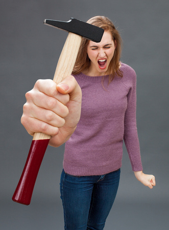 enraged beautiful young woman shouting with a symbolic hammer in hand to express her frustration at DIY, home improvement or repairing with handwork toolの写真素材