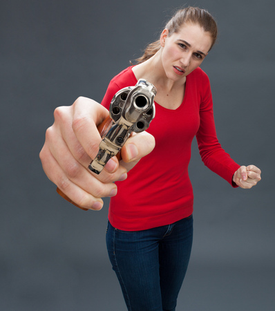 anxious beautiful young woman holding an oversized revolver in the foreground, expressing violence and intimidation with firearmの写真素材