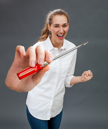 thrilled beautiful young woman smiling with a symbolic screwdriver in hand to express her joy and success at mastering DIY, home improvement or fixing with industrial toolの写真素材