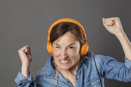 angry middle aged woman frowning with enraged arms raised in listening to noise or music on...