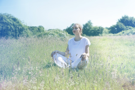 calm beautiful young woman with eyes closed relaxing in green nature, crossing legs for zen yoga and centered mindfulness, soft toned retro effectsの写真素材