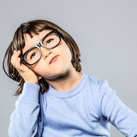 young preschooler with serious eyeglasses holding head for thought, imagination, confusion or headache, grey background studioの写真素材