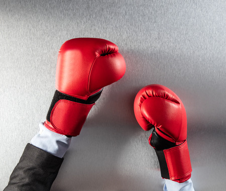 concept of frustration at work or office competition on the workplace for businessman hands with boxing gloves on a metallic empty office desk, top viewの写真素材