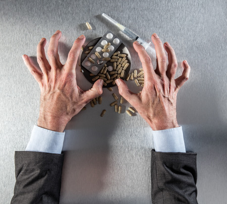 anxious businessman hands expressing stress and frustration for drugs or medicine pills dependency on his office desk for management health or corporate exasperation, above viewの写真素材