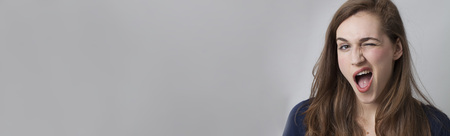 wink, expression and fun concept - sexy young woman winking showing her teeth and long brown hair for success, long banner with copy spaceの写真素材