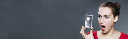 time concept - stunned young woman holding hourglass for concept of time management, panoramic header with copy spaceの写真素材