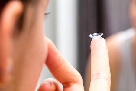 focus of a contact lens held on the finger of a young woman face in a blurred foreground for ophthalmologyの写真素材