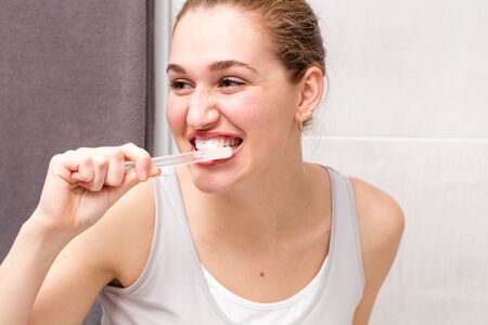 happy healthy dental care and healthcare routine in the bathroom for attractive female teenager brushing and washing her teeth with toothpaste and toothbrush, real peopleの写真素材