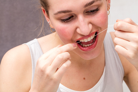 closeup of a beautiful young woman using dental floss to care and clean her teeth for hygiene,...