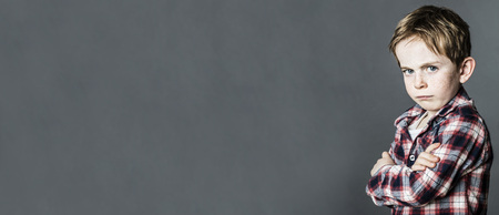 upset little child with freckles standing from profile with arms crossed, pouting and sulking to express his attitude or opposition, contrast effects, long bannerの写真素材