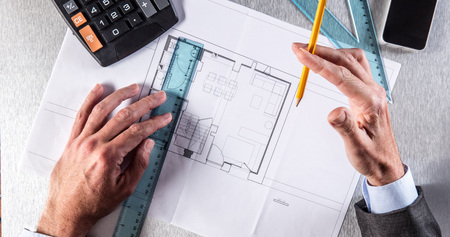 architecture professional hands in reflection, drawing on residential blue print at his desk with calculator, ruler and phone for new property concept, above viewの写真素材