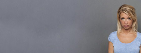 portrait of sad young blond woman looking disappointed, pouting for disillusion and frustration, sulking with a childish funny face, grey copy space long bannerの写真素材