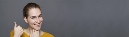 glowing happiness concept - happy 20s girl showing a product up with discreet hand gesture for wellbeing,studio shot on gray copy space bannerの写真素材