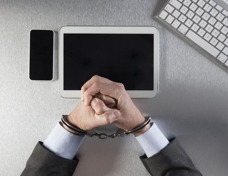 restrained businessman fists tied with handcuffs facing digital technology for concept of modern mobile addiction, hostage or victim of corporate prison, top viewの写真素材