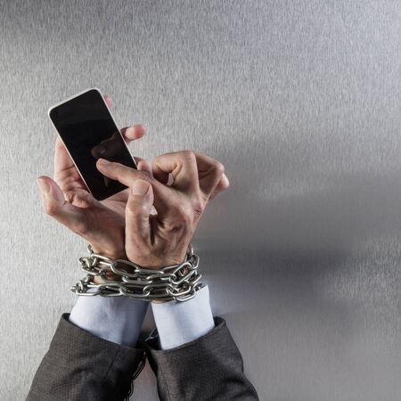 chain tied businessman hands obsessed with his mobile phone for concept of modern communication...