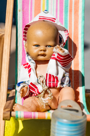 display of a beautiful old summer doll on a small deckchair to recycle and reuse toys or childhood nostalgia at outdoor garage sale, flea market or street fairの写真素材