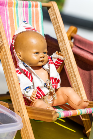 display of an old summer doll on a small deckchair to recycle and reuse toys or childhood nostalgia collector at outdoor garage sale, flea market or street fairの写真素材