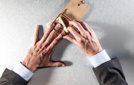 surprised businessman catching corporate money hurt by a mouse trap for company financial trick, danger, bait or strategy question, top viewの写真素材