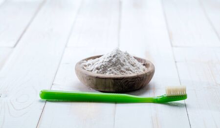 Green toothbrush in the foreground with user friendly baking soda powder in wooden cup for natural dental care on wooden copy space backgroundの写真素材