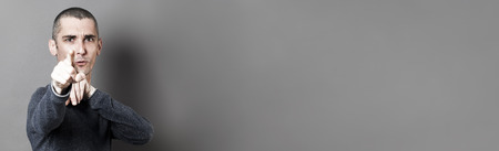 blaming concept - young man with short hair accusing or denouncing someone with his index pointed in the foreground, dark grey long bannerの写真素材