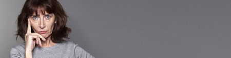 focused mature woman with brown hair and grey sweater thinking,looking concerned and thoughtful, gray bannerの写真素材