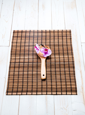 beauty and spa concept with wooden spoon and pink orchid on zen place mat and white board, top view still lifeの写真素材