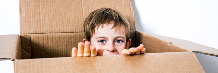 happy little 6 year old child hiding his face in a cardboard box, playing peekaboo or hide and seek for imagination concept, one real personの写真素材
