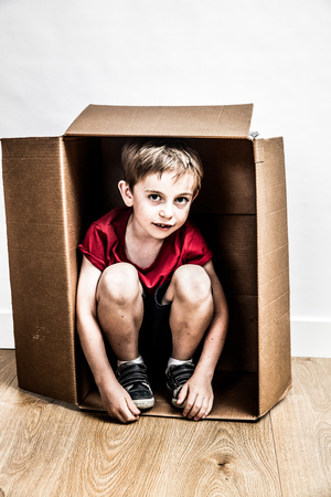 sad 6 year old boy sitting in a small cardboard box hiding for concept of domestic violence, divorce or moving day, one real person, contrast effectsの写真素材