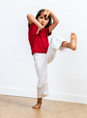 fighting young child raising feet and playing hands to practise martial art, tai chi, kung fu or taekwondo for fun energetic motivation and kid' sport over white backgroundの写真素材