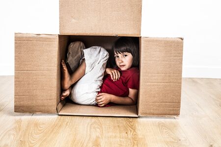 cool child hunched in a tiny cardboard box hiding for protection and confidence from building a small houseの写真素材