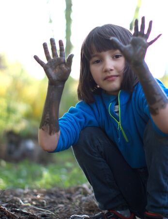 Happy grounded girl smiling, showing muddy hands and arms for fun outdoor learning, playing in...